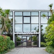 Glass-fronted building entrance labelled BUILDING 41, flanked by tropical plants and palm trees; reflective doors show a street scene.